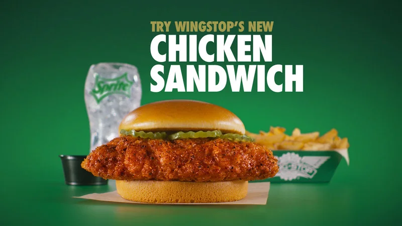 Wingstop Chicken Sandwich with seasoned fries, dip and a Sprite bottle on a green background