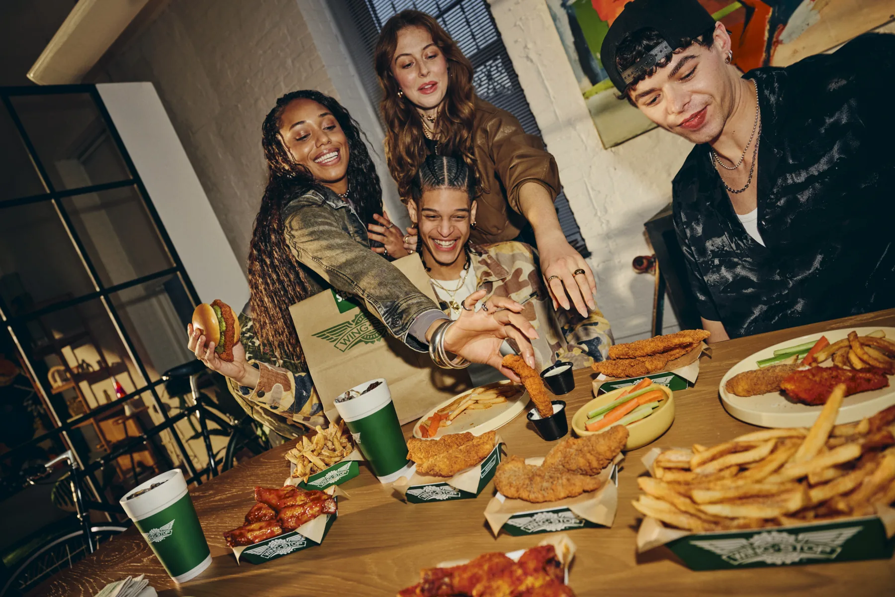 Friends sharing a large Wingstop order with wings, fries and dips